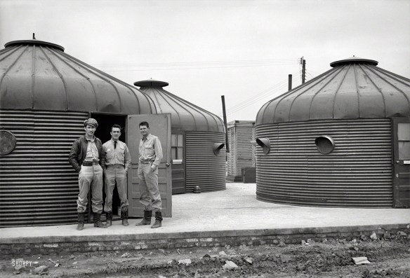 Three U.S. pilots stand in front of a cluster of Dymaxion Deployment Unites, NOrth Africa, 1944